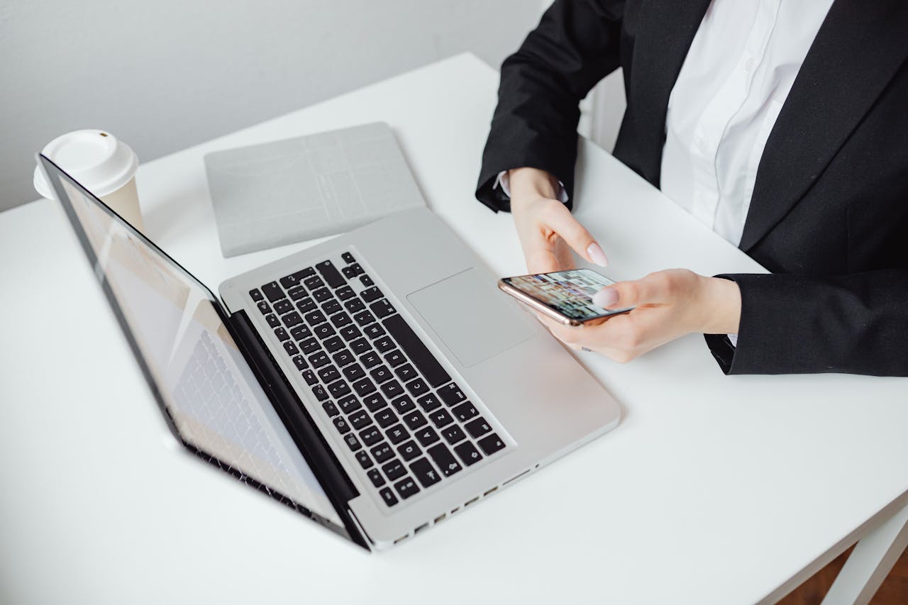 hero-img-02 Businesswoman using smartphone at desk with laptop and coffee cup.